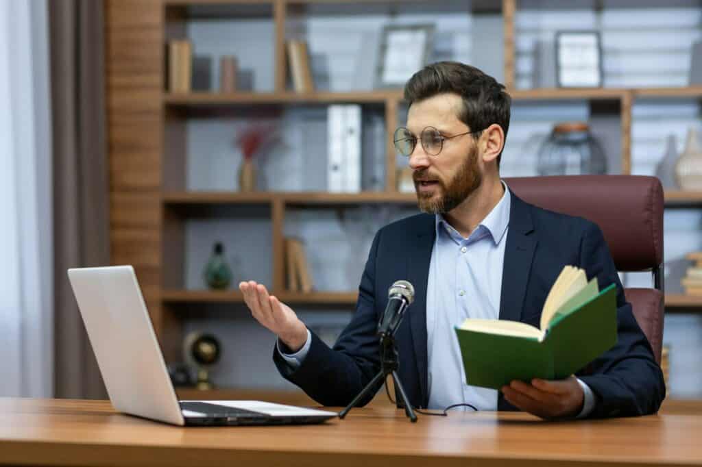 Online presentation of the book. A young man writer, author in a suit sits in the office at a table